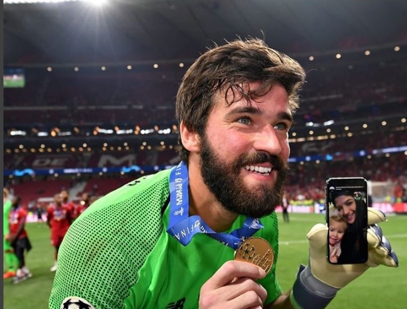 獲歐洲冠軍聯賽，開心地在球場上分享獎牌及手機上妻兒合照。（圖／IG@alissonbecker）